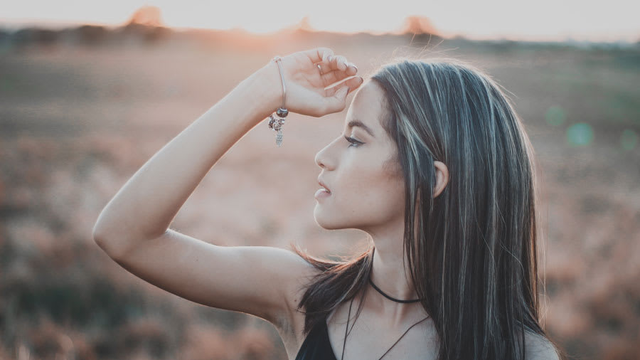 Girl in black tank top raising her arm outside with sunset in background