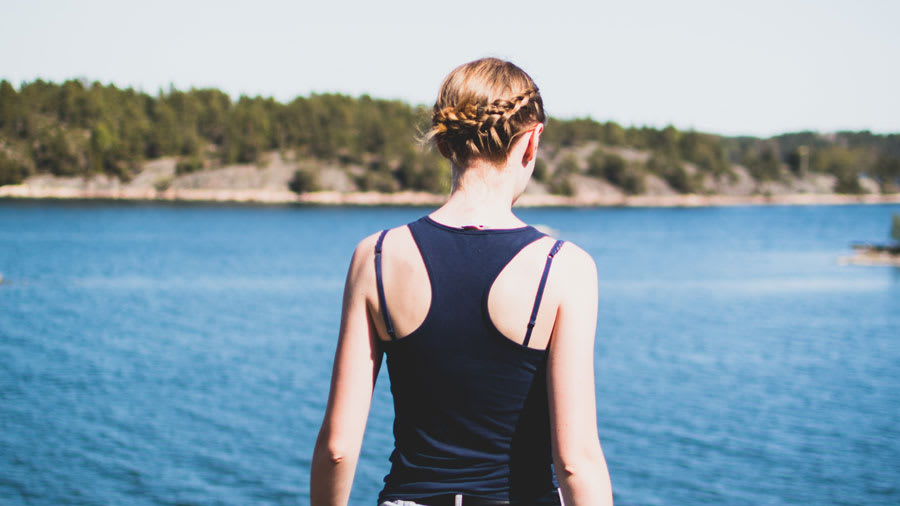 woman with braided hair in front of lake in tank top without acne