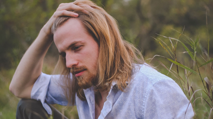 Man with long hair and white shirt placing hand on head