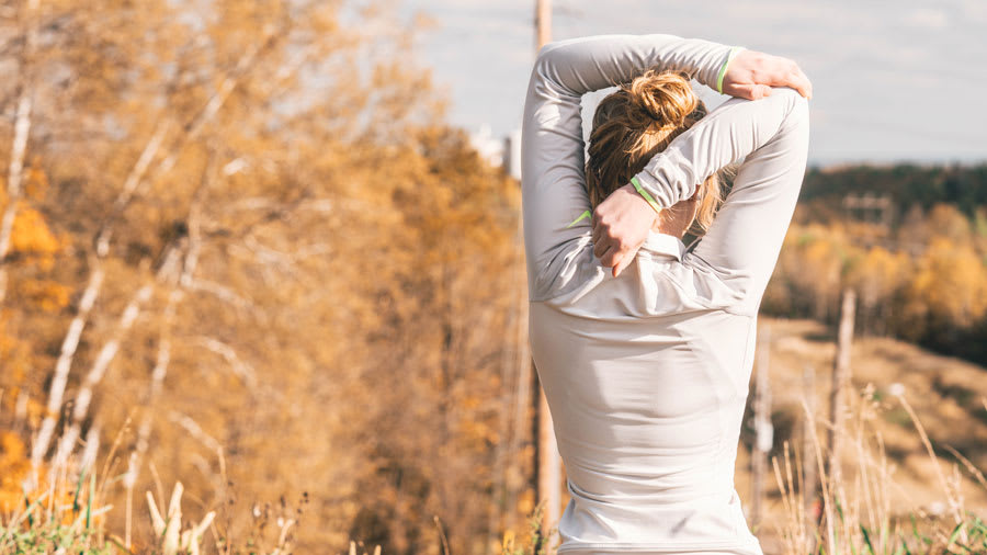Blonde woman stretching arms behind back getting ready to exercise outside