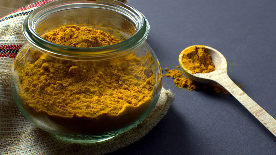Turmeric power in a glass bowl and in a wooden spoon
