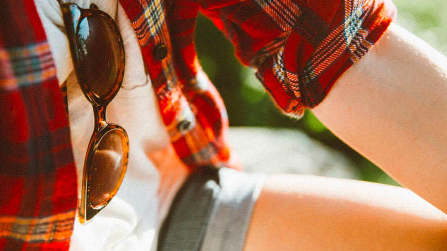 Person in white t-shirt and red flannel and denim shorts with sunglasses hanging from shirt collar