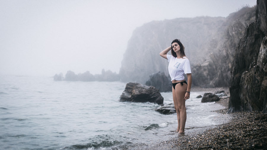 woman in white tee and black bathing suit standing on ocean shore
