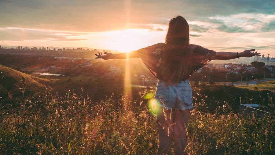 Woman Stands on Mountain with sunset in front of her