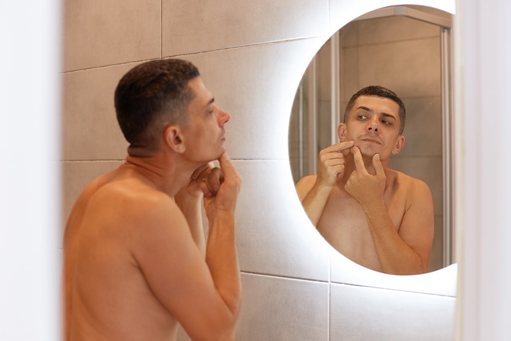 reflection-mirror-handsome-dark-haired-male-standing-with-naked-upper-body-looking-his-face-finds-pimple-having-skin-problems-morning-hygiene-procedures