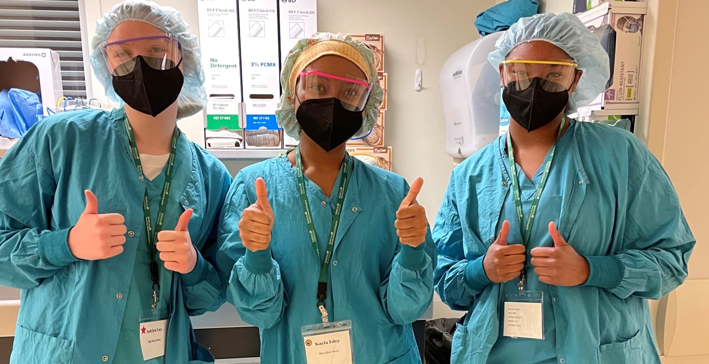 Three M.A.S.H. camp participants dressed in surgical scrubs, masks and protective eye gear.