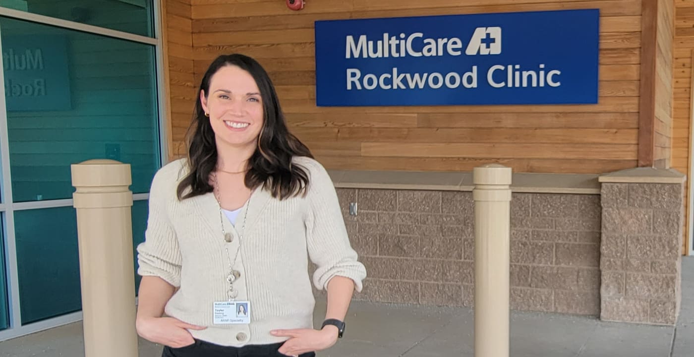 Psychiatric mental health nurse practitioner, Taylor Keating, ARNP, poses in front a building sign reading MultiCare Rockwood Clinic