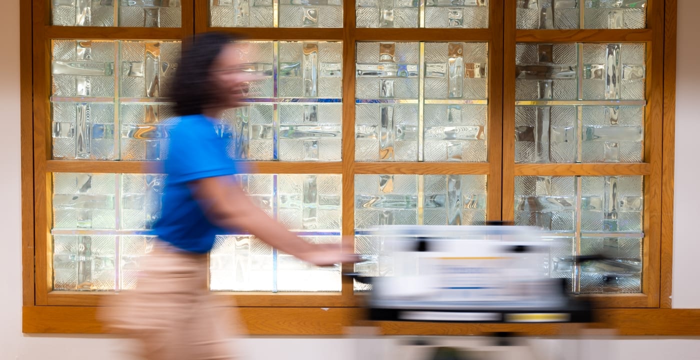 Woman in blue polo and khakis pushes a book cart down a hospital hallway