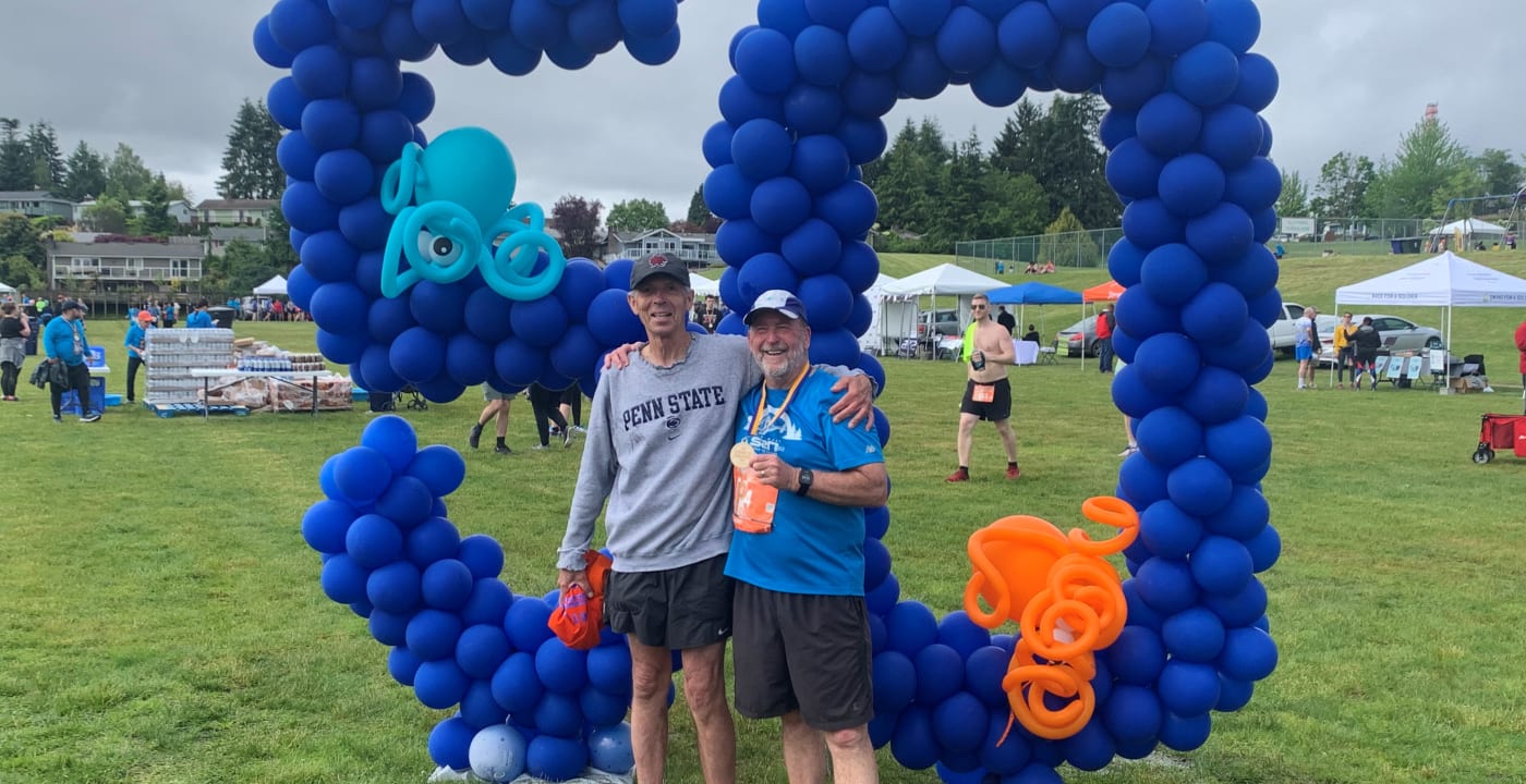 Two man stand side by side in front a “50” balloon decoration in a park