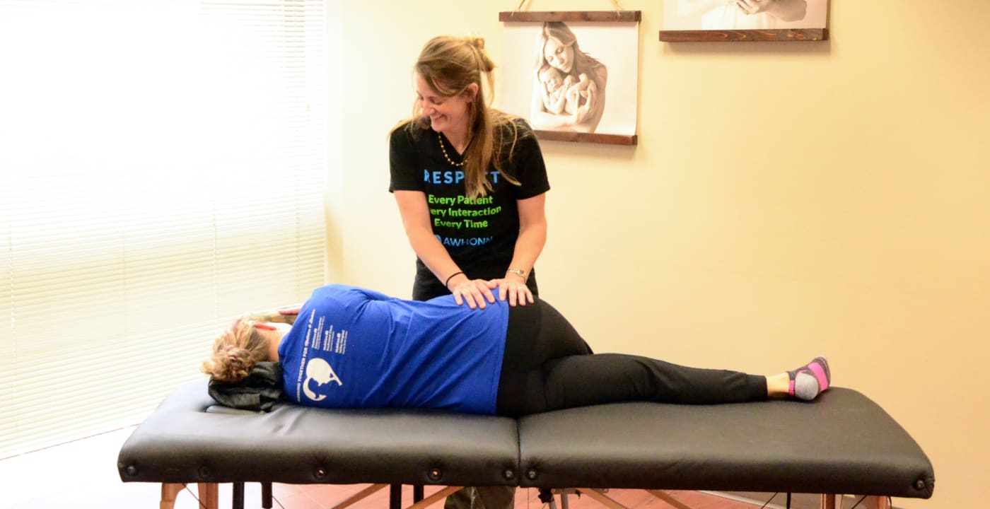 Woman instructs another woman lying on massage table through an exercise