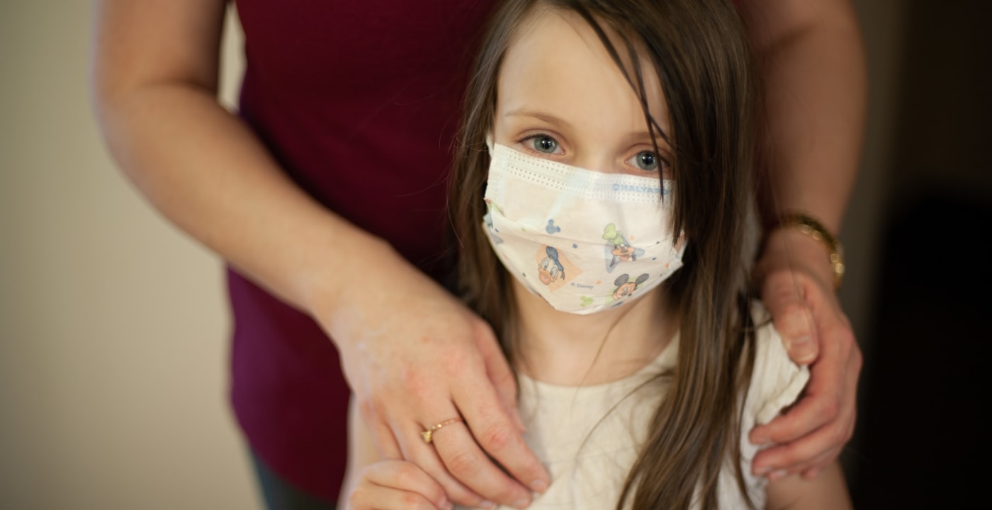 Girl wearing a mask holding the hand of an adult