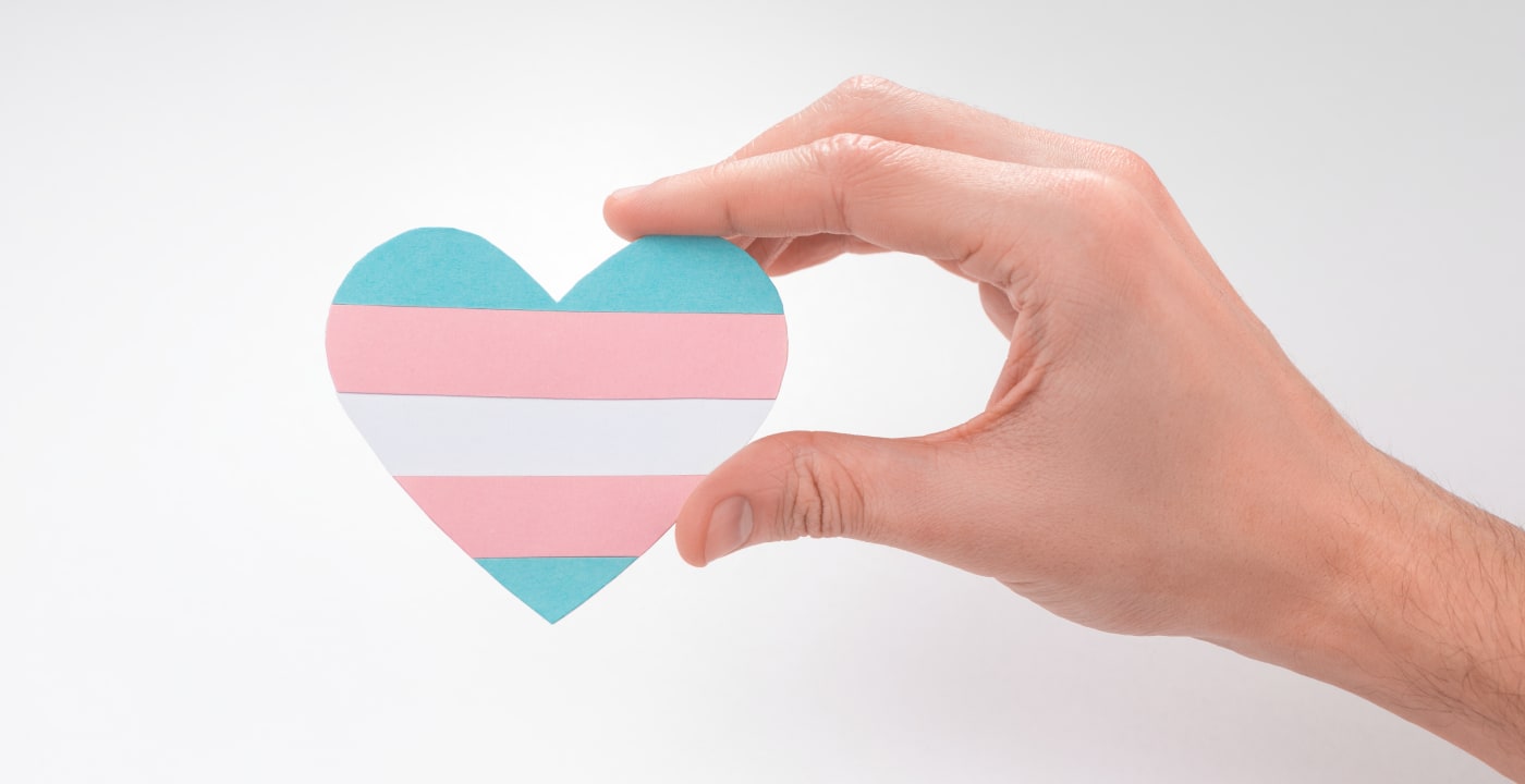 A person’s hand holds a paper heart with the transgender pride colors