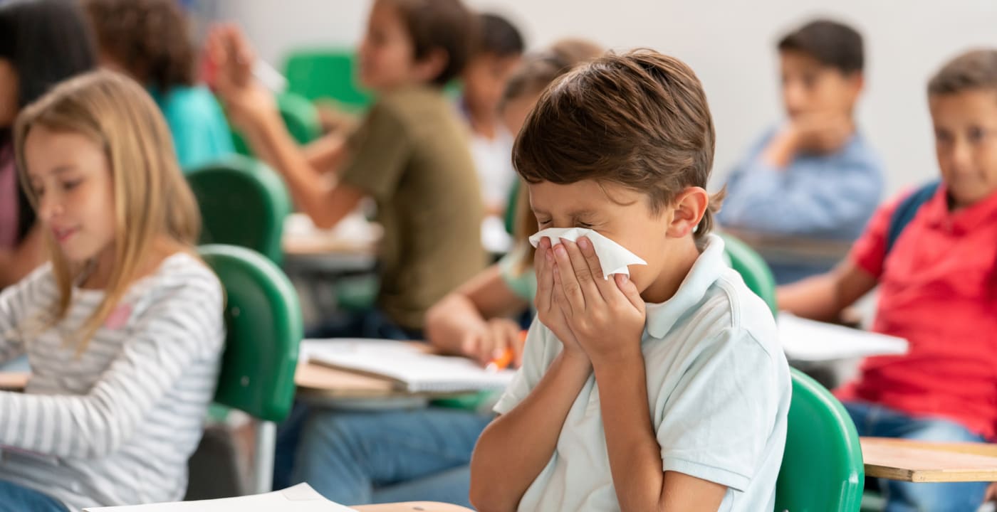 Child blowing nose sitting at classroom desk