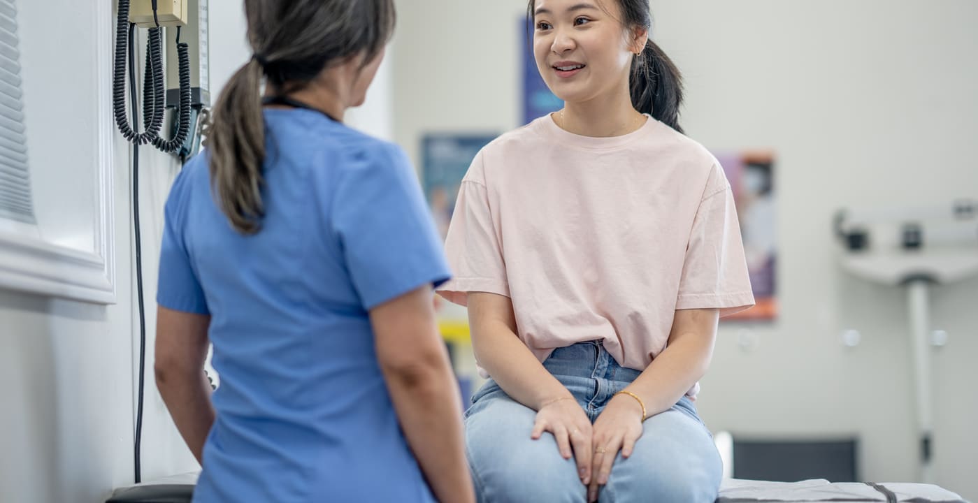 Young girl sits on exam table and talks with provider