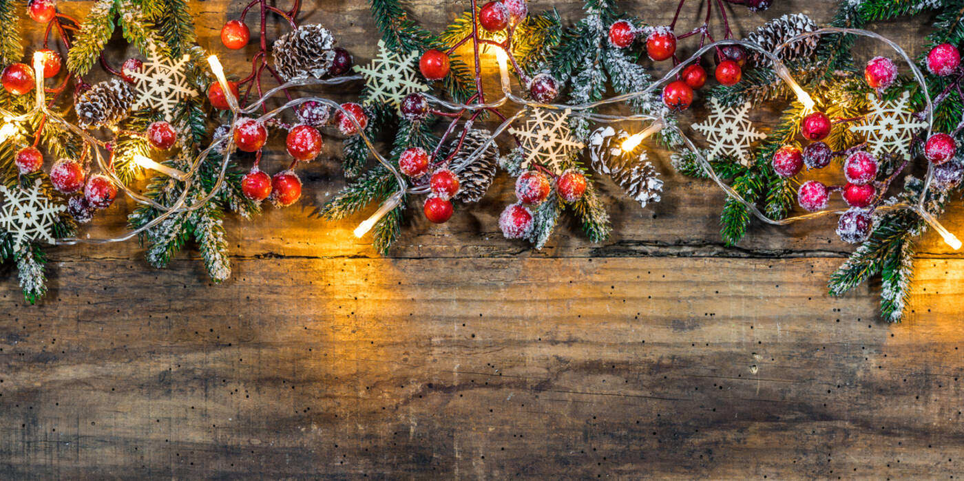 A rough wooden surface decorated with holly, evergreen and white lights