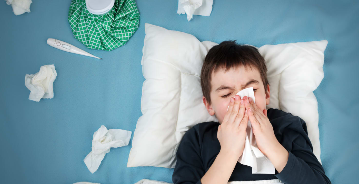 Boy blowing his nose in bed