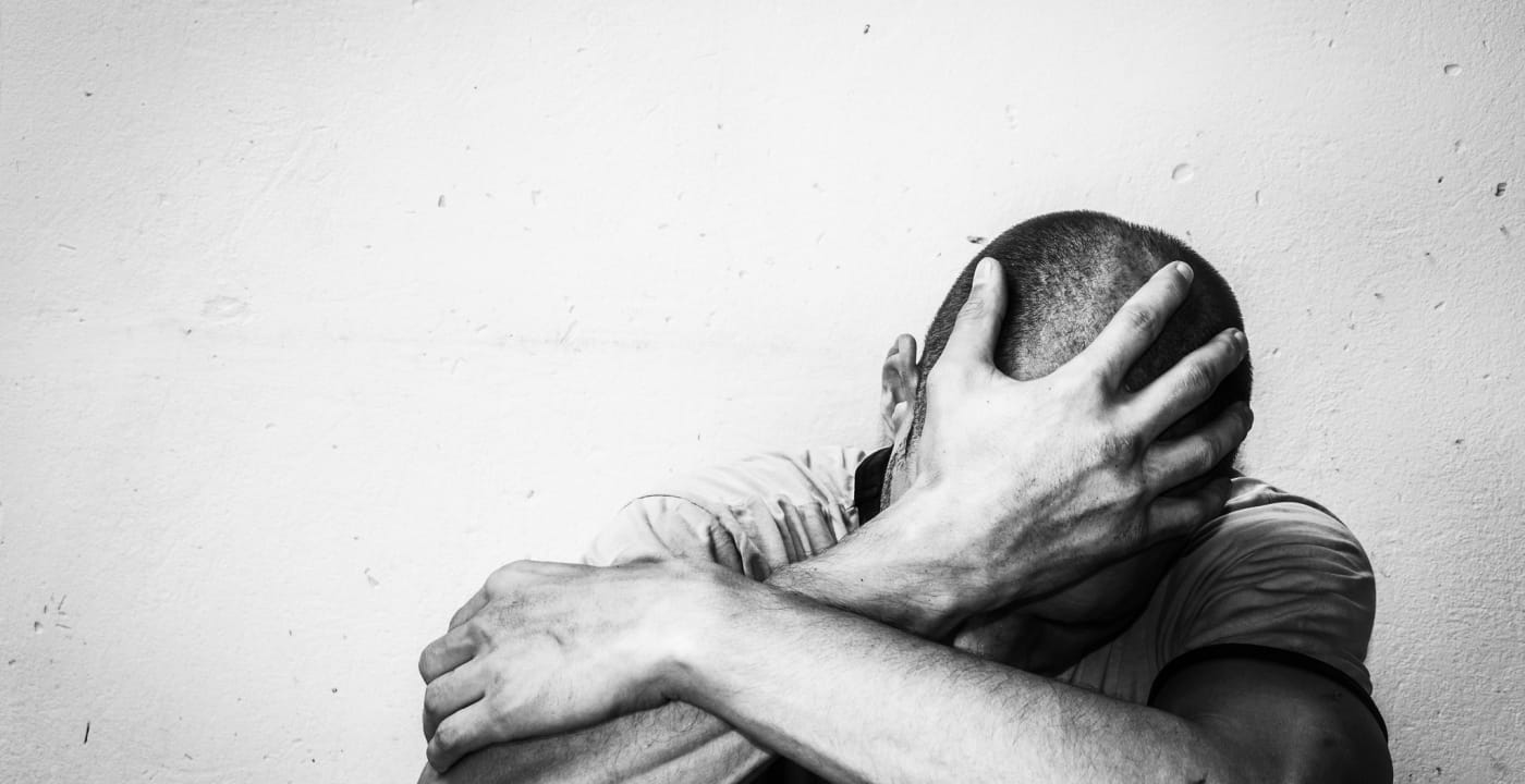 Black and white shot of man sitting and holding head in hand, arms crossed over body