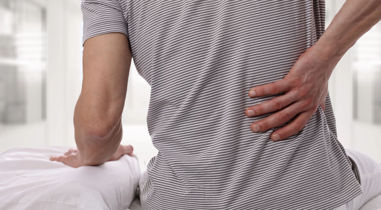 Person sitting on a bed and holding their low back in pain