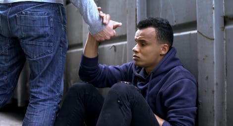 Person offering a hand to a distressed man sitting on the ground