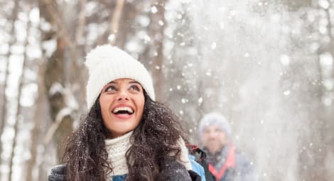 Woman wearing winter hat, scarf and gloves looks up in wonder as it snows around her