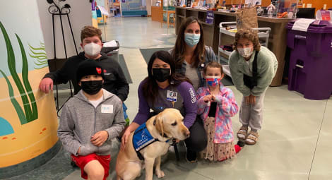 Group of children and adults, plus a golden retriever in a blue vest