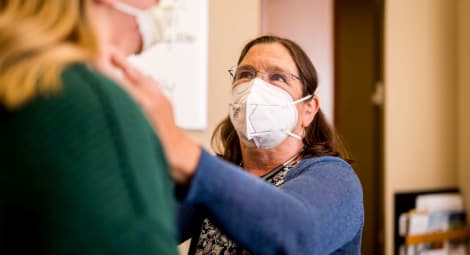 Woman doctor wearing face mask examines blonde patient’s lymph nodes