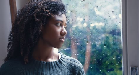 Woman sadly looks out a rain-soaked window