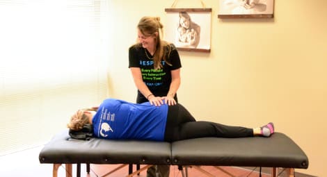 Woman instructs another woman lying on massage table through an exercise