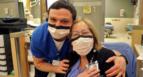 Two MultiCare employees embrace in an emergency department setting. Both are wearing paper masks.