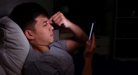 Man scrolling his phone and holding his head.