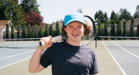 Teen boy in baseball cap poses on tennis court holding a racket