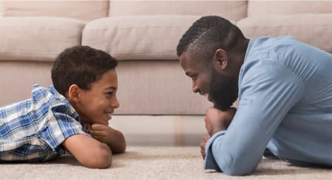 Father and son laying on ground looking at each other