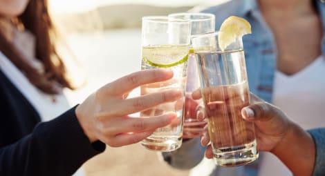 People raising glasses of a clear liquid with lime wedges in a toast