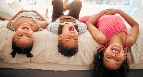 Three children lying upside down on a bed and laughing