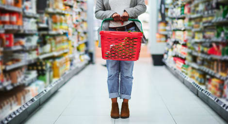 Woman pictured from waist down holding a shopping basket in a grocery store aisle