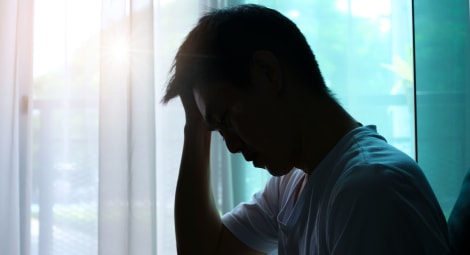 Man sitting in front of a window holding his head with his hand