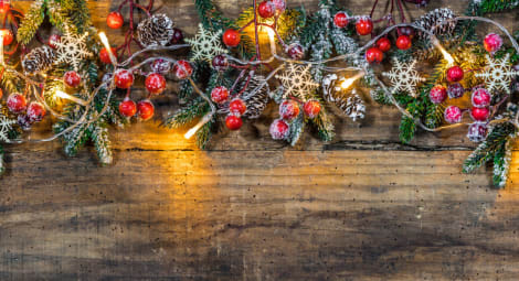 A rough wooden surface decorated with holly, evergreen and white lights