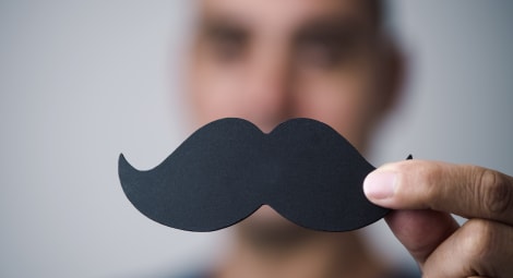 Man holding up a mustache cut out