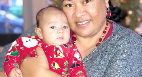 Woman holding her baby in front of a Christmas tree