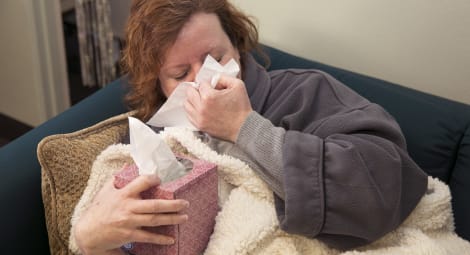 Woman blowing nose while sitting on couch