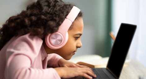 Young girl wearing headphones and squinting at a laptop