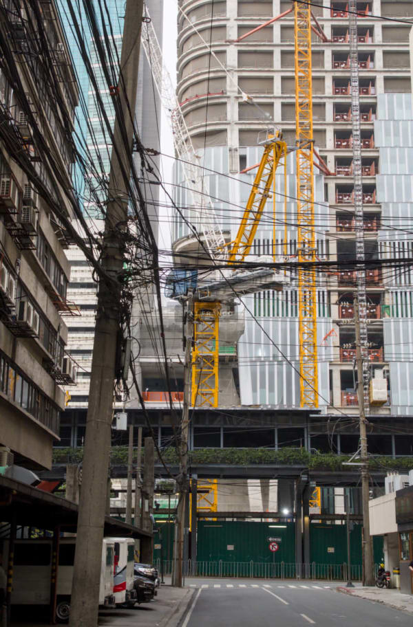 Yellow construction cranes rising above a half-built skyscraper amid a tangle of utility lines in Manila