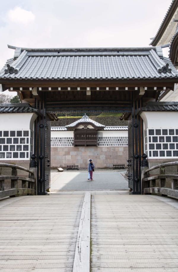 Lone visitor standing at the threshold of Kanazawa Castle's inner Hashizume-mon gate looking through to the stone wall beyond