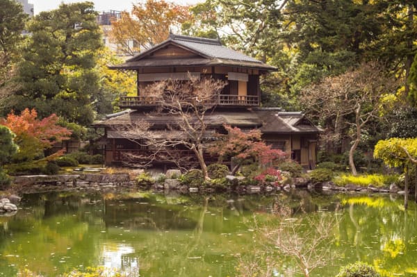 Traditional wooden teahouse reflected in an emerald pond surrounded by autumn foliage in Kenroku-en