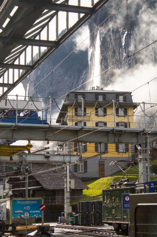 Person in a bonnet hat gazes toward snow-capped peaks and a waterfall cascading into Lauterbrunnen Valley in autumn