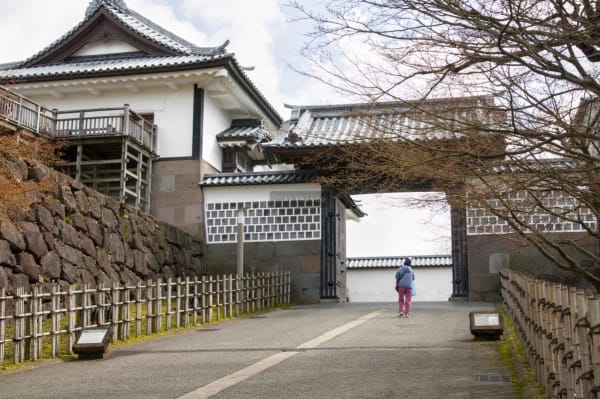 Visitor walks through the bridge approach of Kanazawa Castle's Kahokumon gate with cherry blossom trees beyond