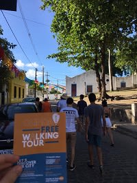 Imagem de panfleto do free walking tour de Olinda, com casario da cidade ao fundo. 