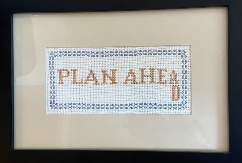 A cross stitch that says 'Plan ahead' where the last part of 'ahead' is scrunched, indicating not enough planning ahead happened to fit all the letters in the space.