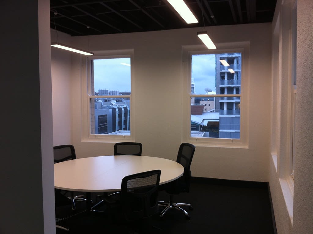 Sala de reuniones vacía de una agencia, con mesa redonda y sillas junto a dos ventanas.