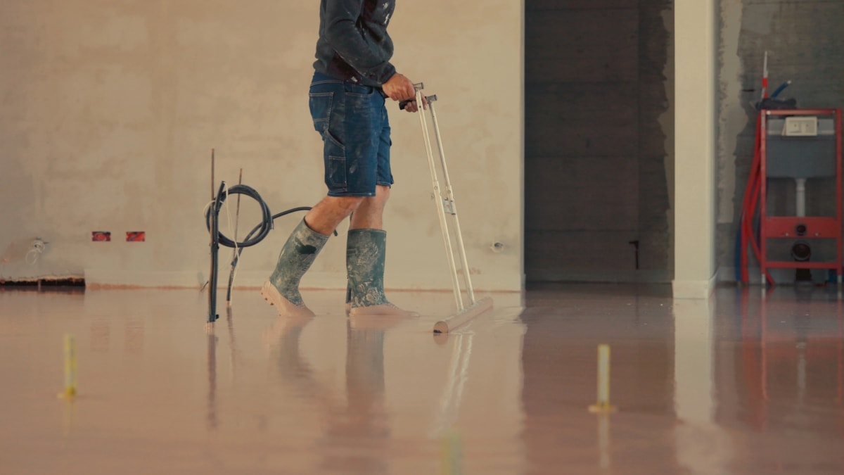 Estrichleger nivelliert Calciumsulfat-Fließestrich mit Schwabbelstange